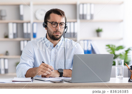 Concentrated serious mature caucasian guy in glasses, headphones work on laptop in living room interior 83616385
