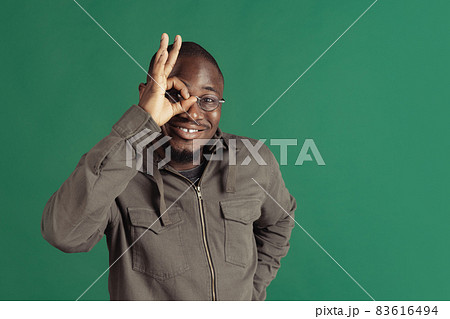 One young stylish african man wearing casual clothes isolated on dark green studio background. Emotions, facial expression concept. One young stylish african man wearing casual clothes isolated on dark green studio background. Emotions, facial expression concept. 83616494