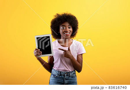 Happy african american lady pointing at digital tablet with blank screen, yellow background, mockup 83616740