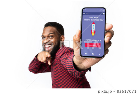 Cheerful young black guy with beard shows finger on phone with website or app about start second business Cheerful young black guy with beard shows finger on phone with website or app about start second business 83617071