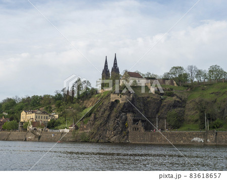 Vltava river bank with view of historical fort Vysehrad with Basilica of St. Peter and Paul, gothic cathedral church on green hill and rock, Prague, Czech republic, spring day. Vltava river bank with view of historical fort Vysehrad with Basilica of St. Peter and Paul, gothic cathedral church on green hill and rock, Prague, Czech republic, spring day. 83618657