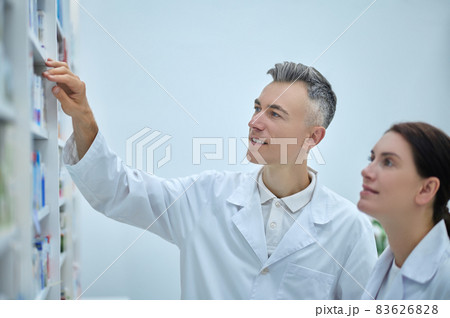 Two pharmacy employees near shelves with medications Two pharmacy employees near shelves with medications 83626828