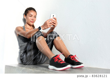 Wearable smart technology devices sport girl lifestyle wearing smartwatch using mobile phone listening to music app with earphones relaxing after fitness workout at gym. Asian woman fit and healthy. Wearable smart technology devices sport girl lifestyle wearing smartwatch using mobile phone listening to music app with earphones relaxing after fitness workout at gym. Asian woman fit and healthy. 83628121
