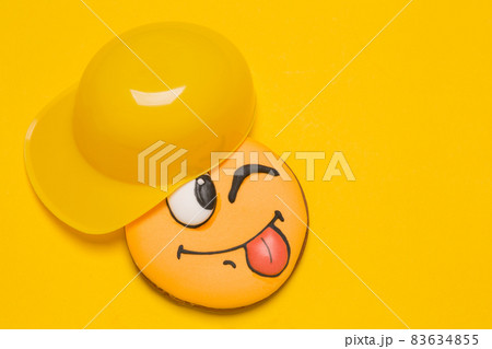 cookie smiley on a yellow background, next to yellow cap baseball cap, baby gingerbread with emotions, concept cookie smiley on a yellow background, next to yellow cap baseball cap, baby gingerbread with emotions, concept 83634855