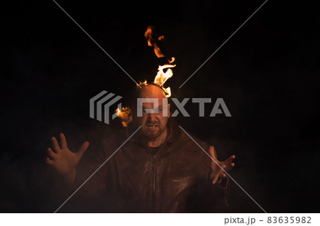 Bald man in a leather jacket with a burning head on a dark background. Bald man in a leather jacket with a burning head on a dark background. 83635982