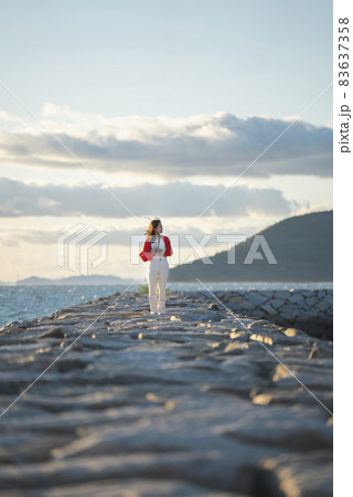夕暮れの海で写真を撮るカメラ女子 83637358