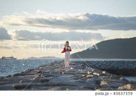 夕暮れの海で写真を撮るカメラ女子 83637359