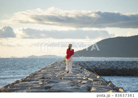 夕暮れの海で写真を撮るカメラ女子 83637361