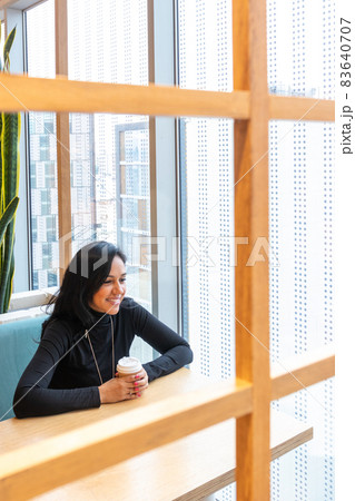 Young brunette woman is drinking coffee and pensively looking out of the street bar window while spending her time alone 83640707