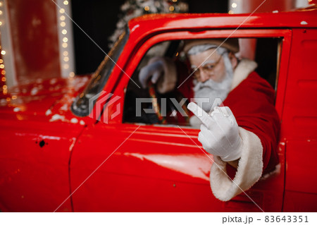 Angry, displeased, annoyed, stylish Santa Claus driving a red car. Santa Claus is preparing for Angry, displeased, annoyed, stylish Santa Claus driving a red car. Santa Claus is preparing for 83643351
