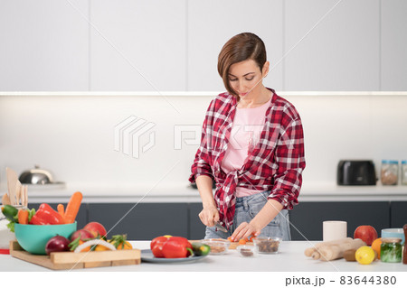 Cooking at home for loving family. Pretty young woman cutting ingredients on table cooking a lunch or dinner standing in the kitchen. Healthy food living. Healthy lifestyle Cooking at home for loving family. Pretty young woman cutting ingredients on table cooking a lunch or dinner standing in the kitchen. Healthy food living. Healthy lifestyle 83644380