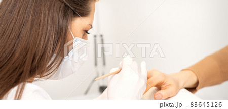 Manicure master in protective face mask and white gloves apply polish to female fingernails. 83645126