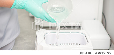 The beautician adds liquid for disinfection of instruments to the machine for sterilization of tools. The beautician adds liquid for disinfection of instruments to the machine for sterilization of tools. 83645195