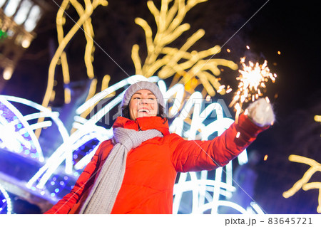 Young beautiful woman in knitted hat and scarf standing in the city with bengal light, sparkler. Concept celebration and christmas. Young beautiful woman in knitted hat and scarf standing in the city with bengal light, sparkler. Concept celebration and christmas. 83645721