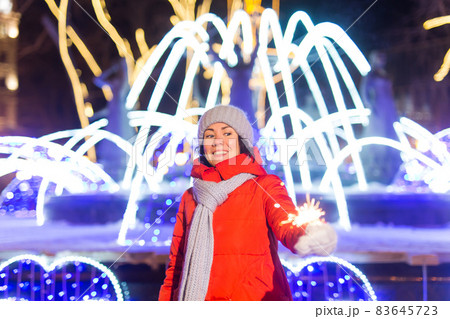 Girl holding a sparkler in her hand. Outdoor winter city background, snow, snowflakes. Girl holding a sparkler in her hand. Outdoor winter city background, snow, snowflakes. 83645723