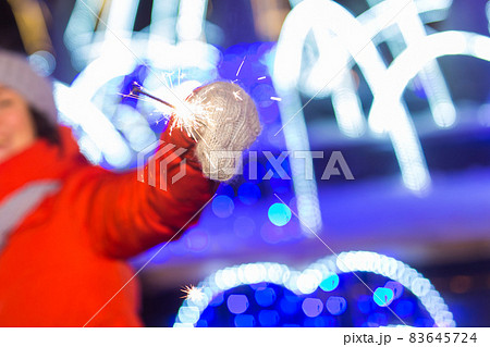 Close-up woman in knitted hat and scarf standing in the city with bengal light, sparkler. Concept celebration and christmas. Close-up woman in knitted hat and scarf standing in the city with bengal light, sparkler. Concept celebration and christmas. 83645724
