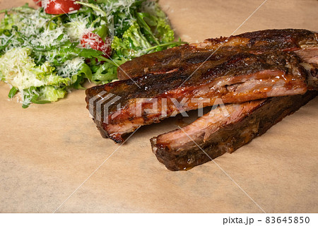 Food cooking. Beef rib with arugula salad with cherry tomatoes and parmesan cheese served on board covered with food grade paper. Restaurant concept Food cooking. Beef rib with arugula salad with cherry tomatoes and parmesan cheese served on board covered with food grade paper. Restaurant concept 83645850
