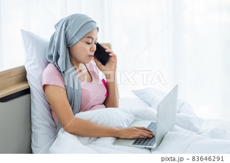 a asian women disease mammary cancer patient hold pick up smartphone casual working with laptop computer with pink ribbon wearing headscarf on bed In the bedroom at the house,healthcare,medicine a asian women disease mammary cancer patient hold pick up smartphone casual working with laptop computer with pink ribbon wearing headscarf on bed In the bedroom at the house,healthcare,medicine 83646291
