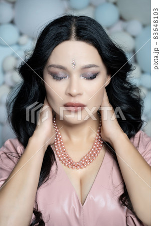 Caucasian Pretty Woman With Closed Eyes Put Her Hands Behind Her Head. Portrait of a Sexy Brunette Lady with Beauty Face. Close-up. Pastel Balls Background 83648103