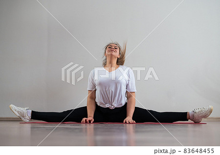 A young flexible fat woman sits in a transverse twine and waves her hair against a white background 83648455