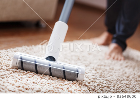 Human legs and a white turbo brush of a cordless vacuum cleaner