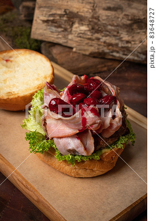 Creative craft burger disassembled with fried slices of bacon and cherry sweet and sour sauce on top, fresh lettuce with lead bun laying next to it. Restaurant concept. Street food concept 83648727