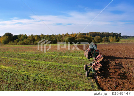 Tractor with Plough on Plowed. Ploughing and Soil Tillage. Agricultural Tractor on Cultivation Field 83649447