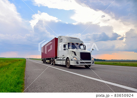 American semi truck transporting sea container on highway on sunset background.  83650924