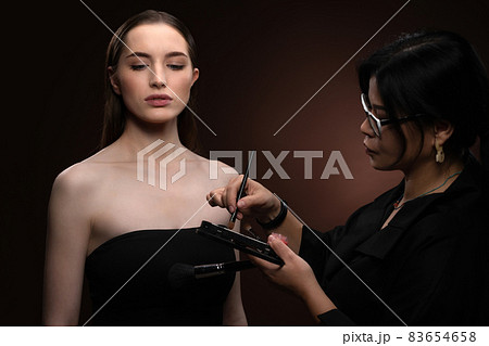 Beauty makeup artist working on a fashion model pretty face isolated on black background. Beautiful model at make up artist. Make-up artist, applying eye shadow to the model Beauty makeup artist working on a fashion model pretty face isolated on black background. Beautiful model at make up artist. Make-up artist, applying eye shadow to the model 83654658