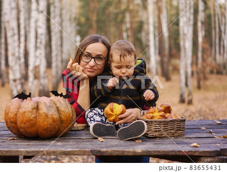 Young woman and her baby son in autumn park, boy playing with helloween pumpkin and eating pumpkin Young woman and her baby son in autumn park, boy playing with helloween pumpkin and eating pumpkin 83655431