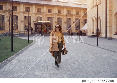 Fashion young woman in sunglasses and hanging on a shoulder autumn beige coat walking on the street happily posing for the camera. Tinted photo Fashion young woman in sunglasses and hanging on a shoulder autumn beige coat walking on the street happily posing for the camera. Tinted photo 83657206