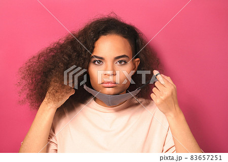 No emotion or indifference holding reusable mask African American girl in peachy t-shirt, to prevent others from corona COVID-19 and SARS cov 2 infection isolated on pink background No emotion or indifference holding reusable mask African American girl in peachy t-shirt, to prevent others from corona COVID-19 and SARS cov 2 infection isolated on pink background 83657251