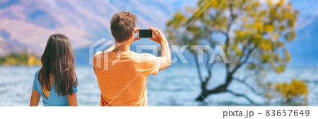 Travel lifestyle people tourists taking picture with phone on New Zealand Wanaka tree background Vacation couple banner panorama. Travel lifestyle people tourists taking picture with phone on New Zealand Wanaka tree background Vacation couple banner panorama. 83657649