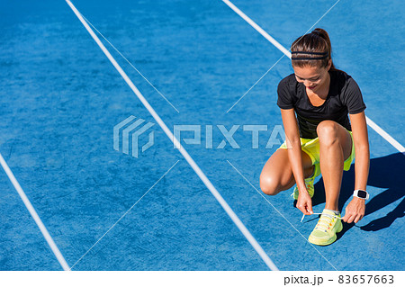 Sprinter runner getting ready to run on running lanes in track and field stadium outside. Woman athlete tying shoe laces for competition on blue tracks Sprinter runner getting ready to run on running lanes in track and field stadium outside. Woman athlete tying shoe laces for competition on blue tracks 83657663