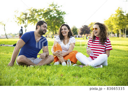 Three friends sitting on the grass in the park 83665335