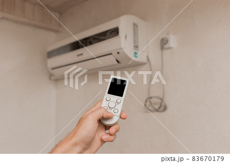 The guy's hand holds the remote control of the air conditioner. Cooling and temperature control in the room of the house 83670179