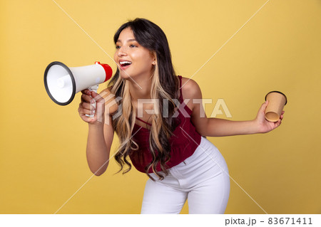 Portrait of young beuatiful girl, student in casual style clothes shouting at megaphone isolated on yellow studio backgroud. 83671411