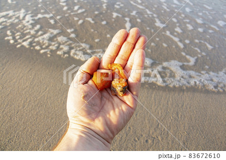 Beautiful pieces of amber in the hand of the sea background. A glowing wavy piece of amber in the palm of your hand. The sunstone. Beautiful pieces of amber in the hand of the sea background. A glowing wavy piece of amber in the palm of your hand. The sunstone. 83672610