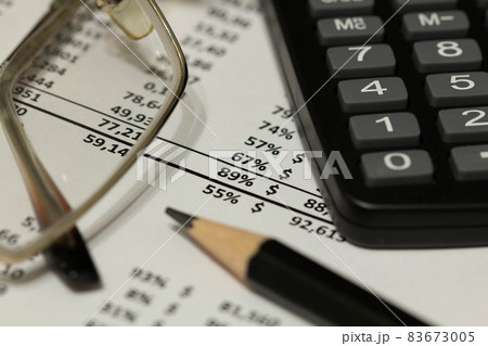 Financial report, calculator, glasses and pencil on the table in the office. A paper sheet full of business data. Accounts number on the data paper. Business documents on office table. Closeup. Financial report, calculator, glasses and pencil on the table in the office. A paper sheet full of business data. Accounts number on the data paper. Business documents on office table. Closeup. 83673005
