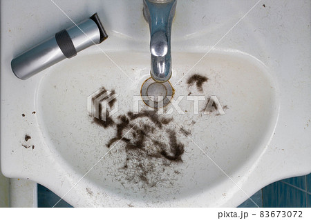 Dirty Bathroom sink with hair after shaving and wireless electric razor. Freshly cut hair from the head, beard and mustache. Water Mixer Tap. Clogged and blocked. Copy space for text. Top view Dirty Bathroom sink with hair after shaving and wireless electric razor. Freshly cut hair from the head, beard and mustache. Water Mixer Tap. Clogged and blocked. Copy space for text. Top view 83673072