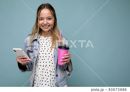 Photo closeup of gorgeous pretty woman in jean jacket smiling and holding smartphone while drinking Photo closeup of gorgeous pretty woman in jean jacket smiling and holding smartphone while drinking 83673886