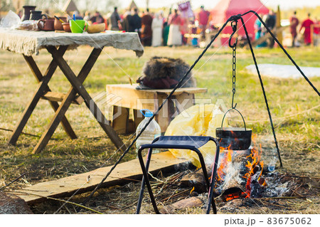 Camping outdoors - tents, equipment and cooking. Cooking at a camping site in nature. The bowler is basking in the fire. Camping outdoors - tents, equipment and cooking. Cooking at a camping site in nature. The bowler is basking in the fire. 83675062