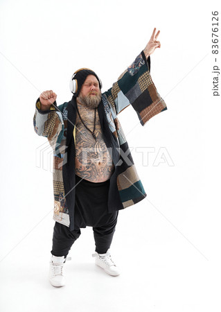 Fat stylish bearded tattoed caucasian man with big belly is posing and dancing wearing ethnic kimono 83676126