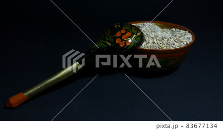 Raw pearl barley in a wooden dish with folk patterns and a wooden spoon lying on a bowl Raw pearl barley in a wooden dish with folk patterns and a wooden spoon lying on a bowl 83677134