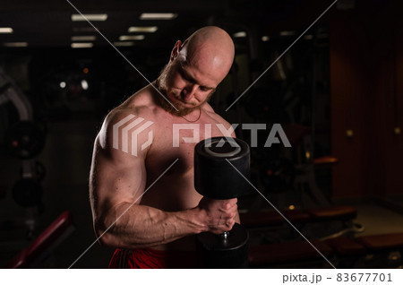 Shirtless handsome man doing biceps and triceps exercises with dumbbell. Embossed bodybuilder with a beautiful body. Muscular trainer in the gym. 83677701