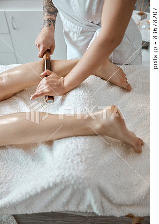 Conident female specialist is doing leg massage with bamboo stick to beautiful caucasean woman client Conident female specialist is doing leg massage with bamboo stick to beautiful caucasean woman client 83678207