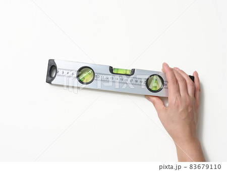 female hands holds a gray metallic building level on a white background. Measuring instrument female hands holds a gray metallic building level on a white background. Measuring instrument 83679110