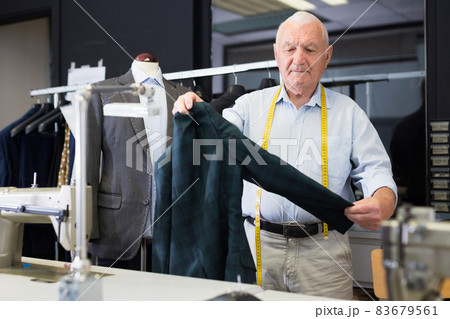 Professional tailor inspects mens jacket before starting work in workshop Professional tailor inspects mens jacket before starting work in workshop 83679561