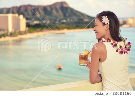 Hawaii vacation summer travel- Mai Tai and aloha spirit. Asian woman relaxing drinking Hawaiian cocktail drink Mai Tai, at sunset view of Waikiki beach in Honolulu, Oahu, USA travel. 83681160
