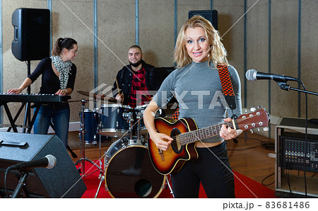 Attractive female soloist playing guitar and singing with her music band in sound studio Attractive female soloist playing guitar and singing with her music band in sound studio 83681486